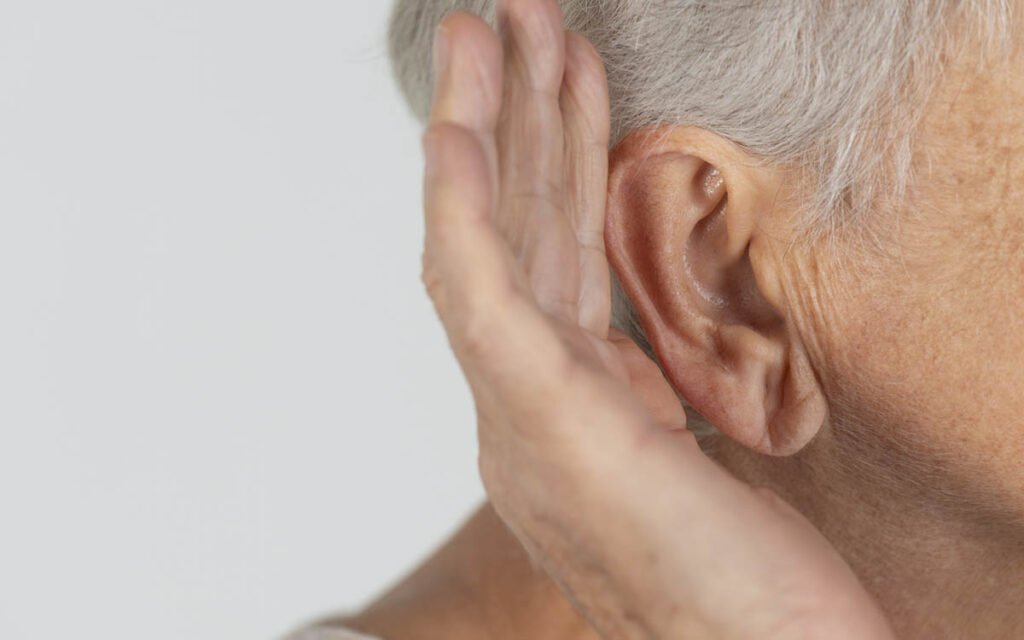 An old woman with her hand up to her ear.